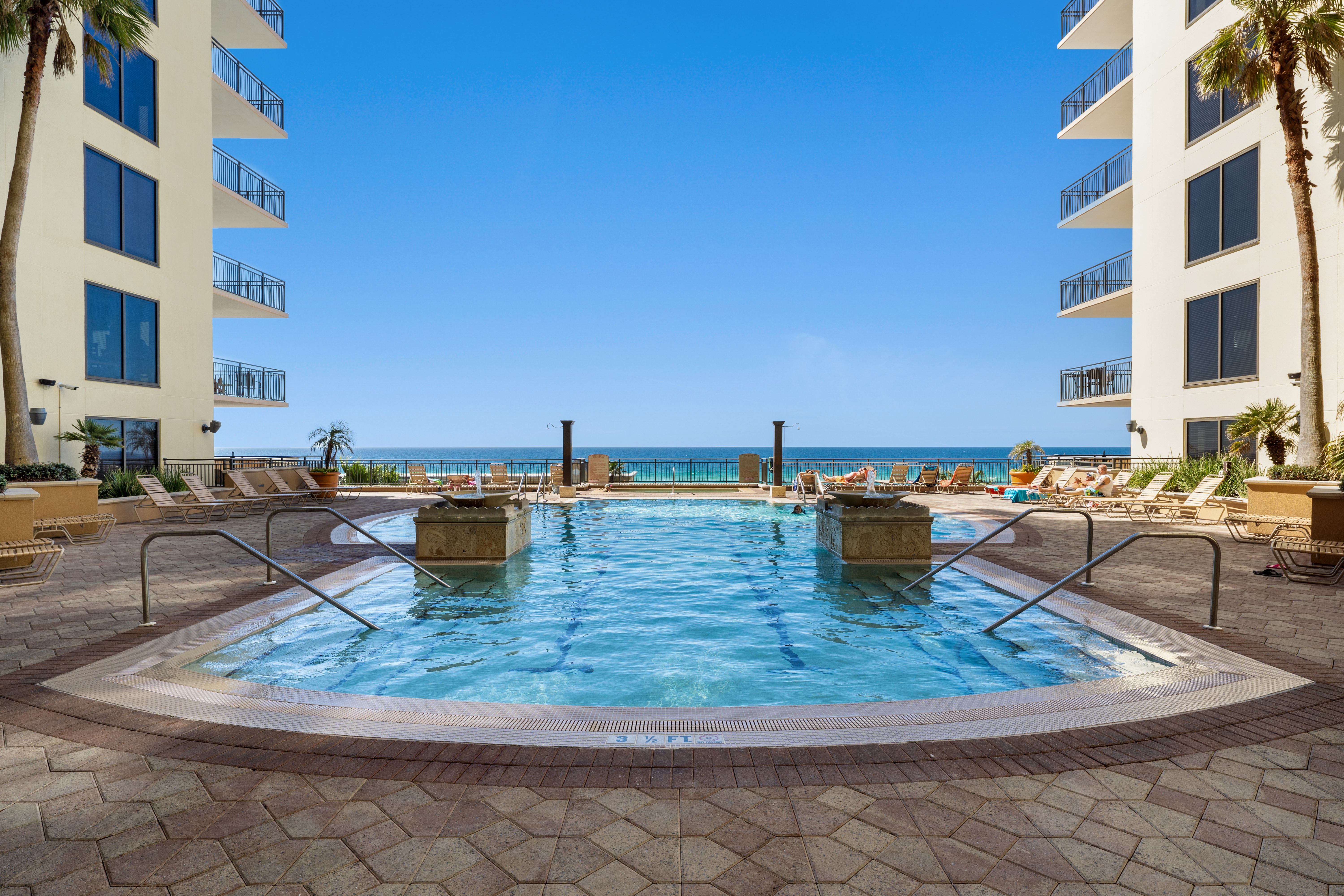 A pool area with a large pool, lounge chairs, and buildings in the background.